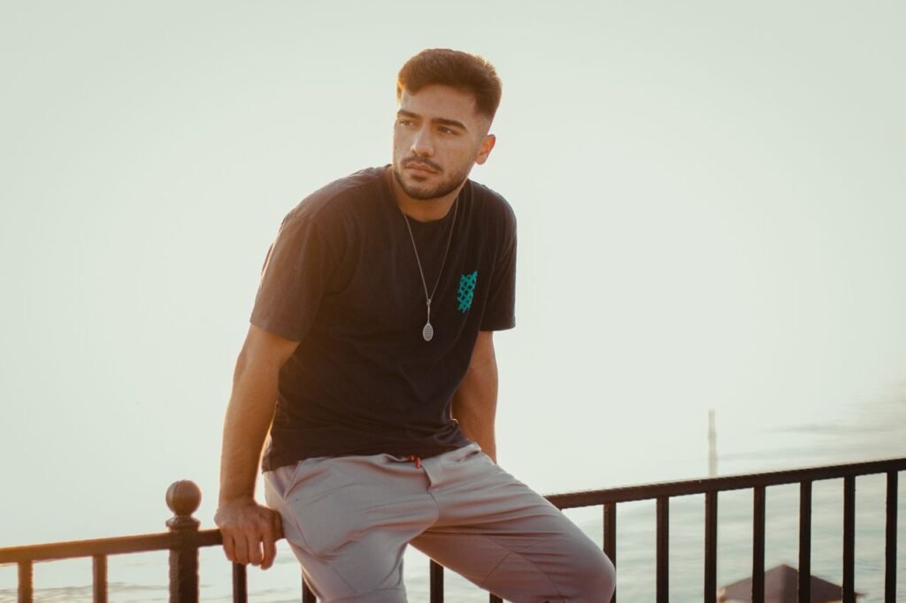 A contemplative young man in casual attire sits by a lakeside railing at Mollakasım, Van.