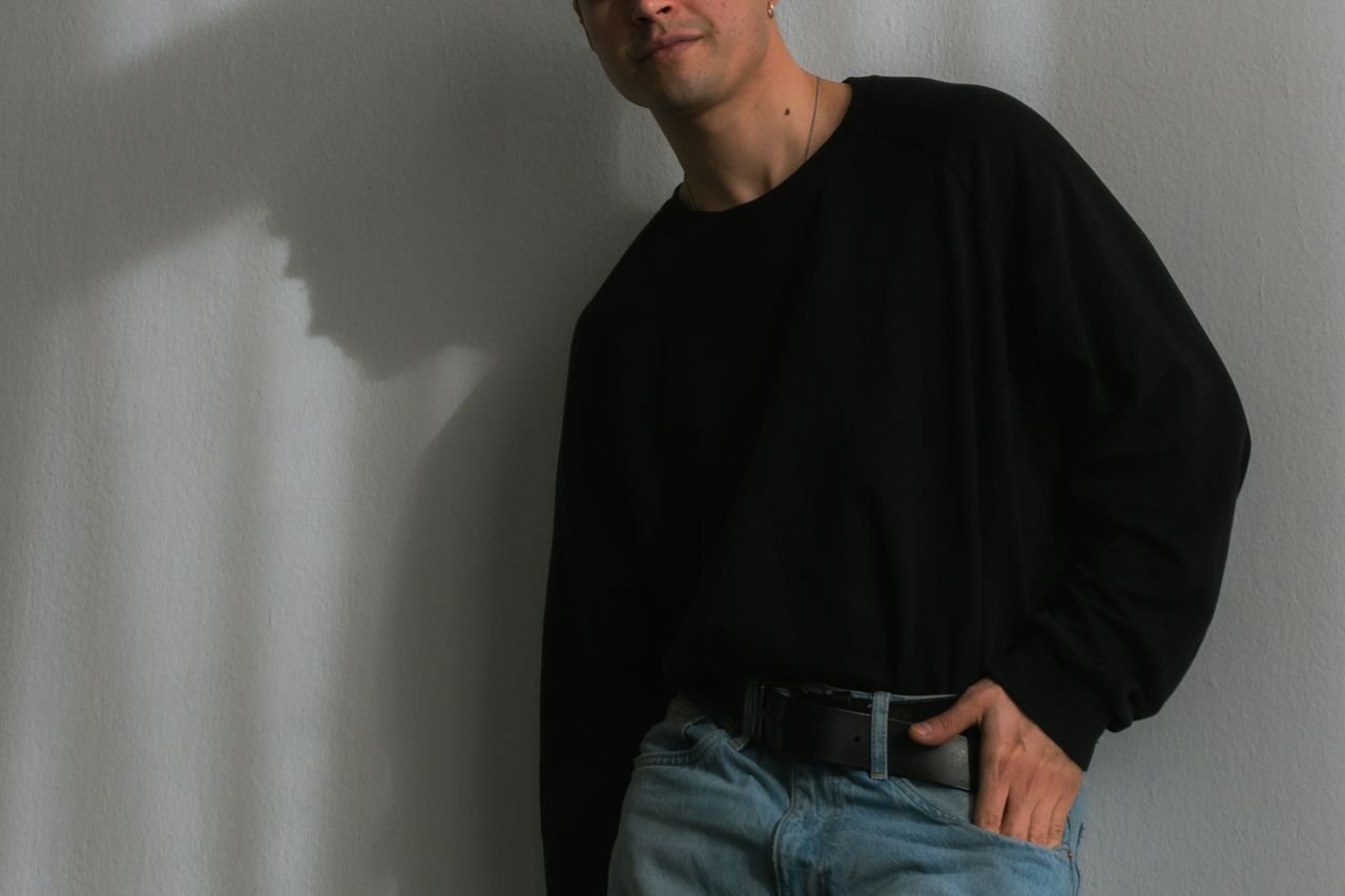 Fashionable male model posing with a casual hand-in-pocket look against a white wall.