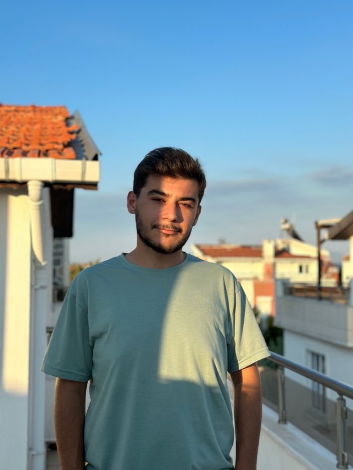A young man stands on a balcony basking in the warm golden hour light with a serene urban backdrop.