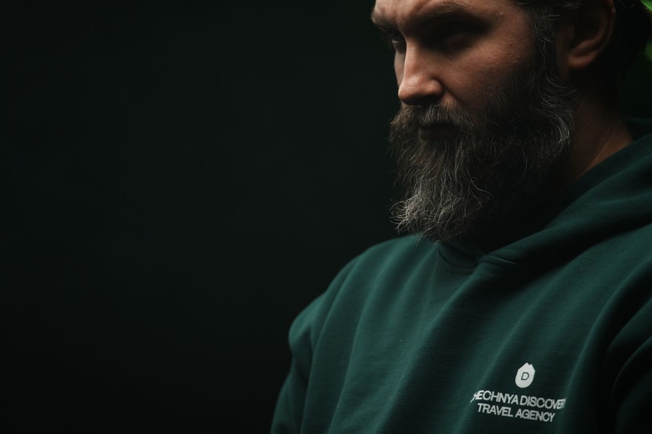Thoughtful bearded man wearing a dark green hoodie in a moody, low-light setting.